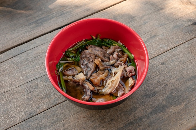 Combinazione di zuppa di noodle di manzo e frattaglie con verdure in una ciotola rossa su un tavolo di legno in un ristorante locale