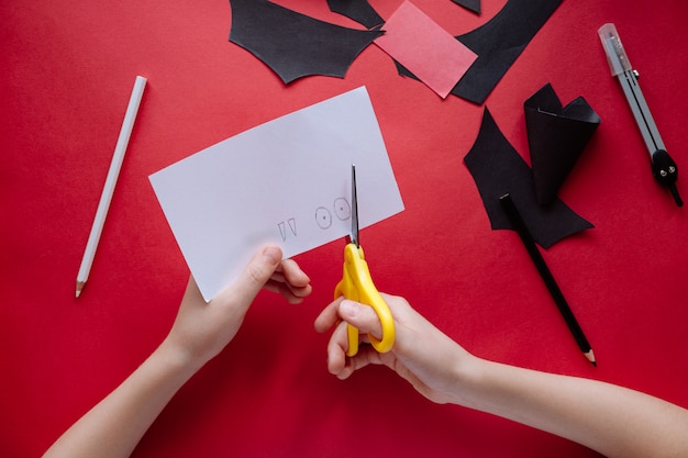 Come fare pipistrello di carta a casa. Mani che fanno mestiere di carta. Istruzioni fotografiche passo dopo passo. Passaggio 8. Taglia gli occhi e le zanne. Progetto artistico fai-da-te per bambini.