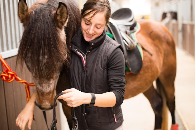 Come usare la museruola della briglia del cavallo La donna di età media si prepara nella scuola di equitazione per l'allenamento