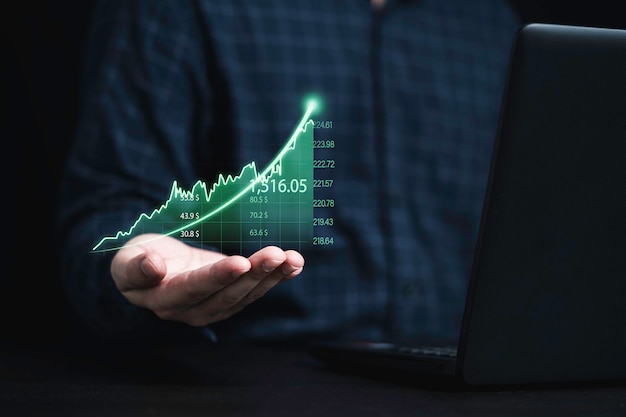 Commerciante che tiene il grafico grafico verde con la freccia e utilizza il computer portatile per l'analisi delle informazioni sul mercato azionario, concetto di investimento.