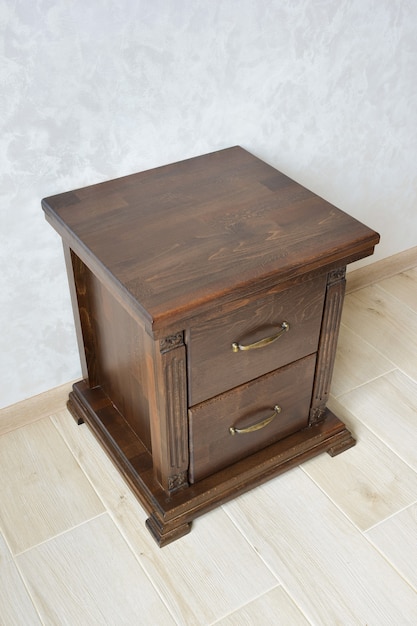 Comodino decorativo in legno marrone con due cassetti vicino alla parete su un pavimento piastrellato. Per gli accessori da comodino