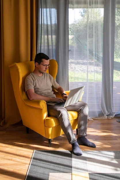 Comodo ufficio a casa Un uomo è seduto e lavora in una grande poltrona gialla in un luminoso appartamento loft