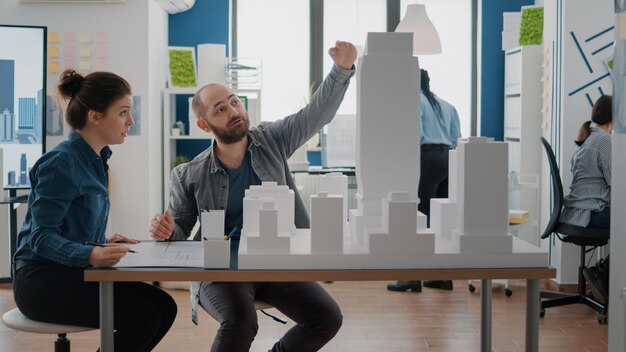 Compagni di lavoro che esaminano il modello di edificio per progettare progetti architettonici per il progetto di costruzione. Uomo e donna che lavorano insieme per pianificare la struttura urbana e il layout per lo sviluppo.