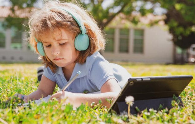 Compiti per bambini fuori nel cortile di scuola piccolo allievo scolaro con tablet nel parco sull'erba auto e