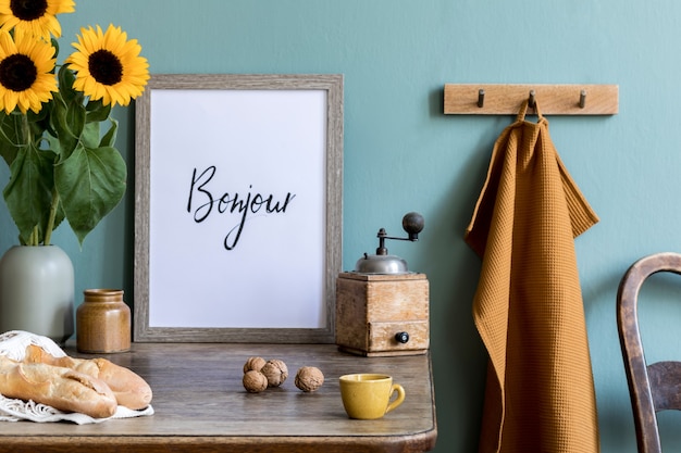 Composizione accogliente ed elegante di sala da pranzo creativa con cornice poter, consola in legno, girasoli e accessori personali. Muro verde. Mattinata bella e soleggiata.