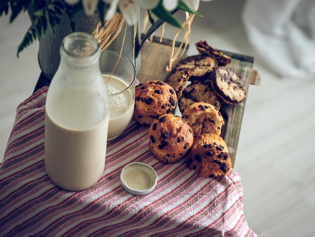 Composizione ad alto angolo di deliziosa pasticceria fatta in casa e bottiglia di latte posta vicino al vaso con fiori su scatola di legno con panno