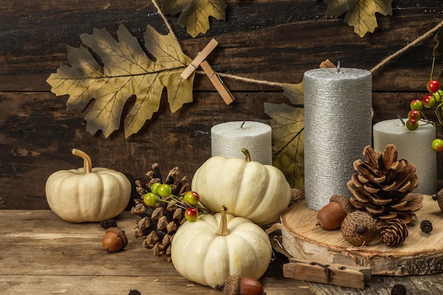 Composizione autunnale con decori tradizionali. Zucche bianche, candele, foglie autunnali, ghiande, coni. Sfondo di tavole di legno, copia spazio