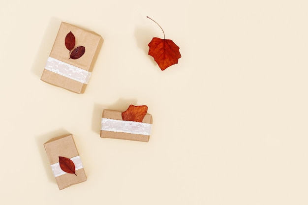 Composizione autunnale con foglie autunnali rosse e scatole regalo festive fatte a mano su beige neutro