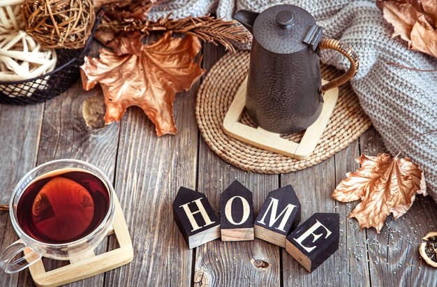 Composizione autunnale con una tazza di tè, teiera e parola casa in legno.