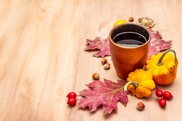 Composizione autunnale di umore accogliente. Tè caldo in vetro ceramico, foglie di autunno, zucche, radica, nocciole