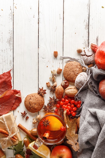 Composizione autunnale di una tazza di tè caldo foglie di autunno frutti e spezie su un tavolo di legno bianco