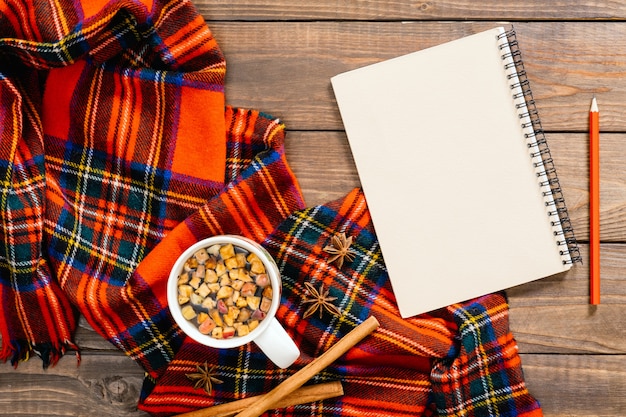 Composizione autunnale flatlay. Sciarpa moda donna rossa, blocco note in carta vintage, tazza da tè, penna, stecca di cannella