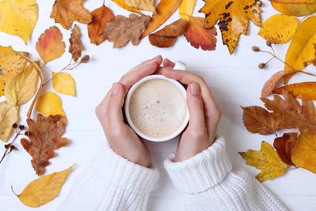 Composizione autunnale vista dall'alto tazza di caffè nelle mani e foglie d'autunno