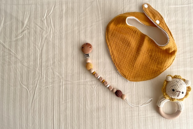 Composizione con bavaglini in mussola baby sonagli con corpino in maglia e catene di perline di legno con molletta per capezzoli su sfondo chiaro