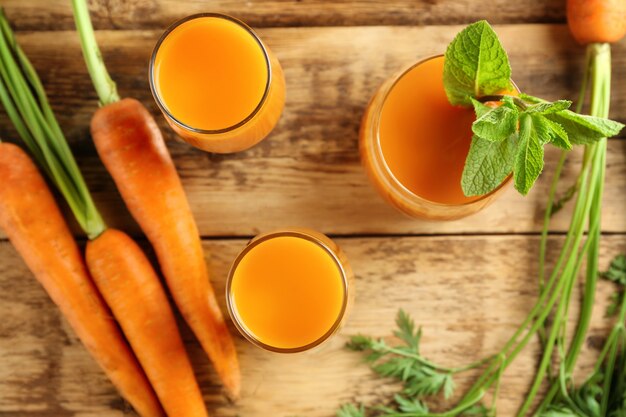 Composizione con bicchieri di succo di carota fresca e verdure sulla tavola di legno