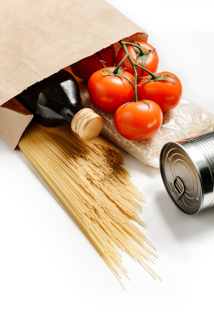 Composizione con borsa artigianale, spaghetti, pomodori, riso, conserve e olio d'oliva isolato su un muro bianco.