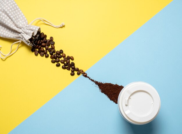 Composizione con caffè. i chicchi di caffè fuoriescono da un sacchetto su sfondi gialli e si trasformano in caffè macinato su sfondi blu. Disposizione piana, vista dall'alto, copia spazio