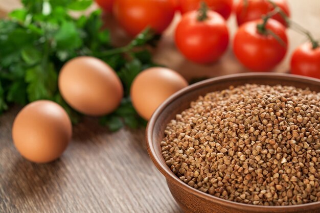 Composizione con ciotola in ceramica secca di grano saraceno, uova, pomodori e prezzemolo sullo sfondo.