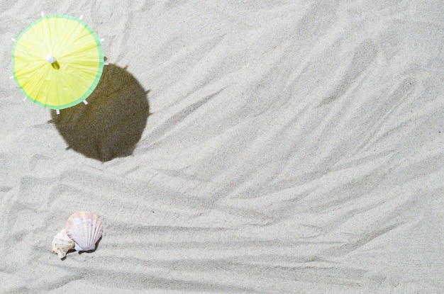 Composizione con conchiglie e ombrellone sulla sabbia di mare Concetto di viaggio e vacanza