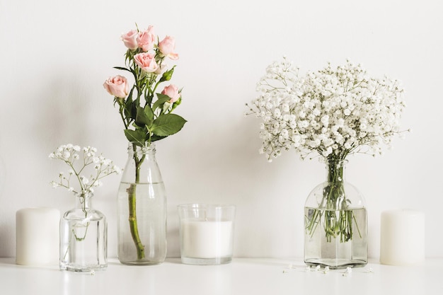 Composizione con fiori bianchi e rosa in bottiglie di vetro e candele sullo sfondo della parete del tavolo.