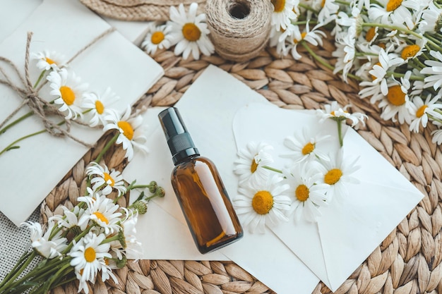 Composizione con fiori di camomilla e bottiglia cosmetica di olio essenziale su sfondo bianco vista dall'alto