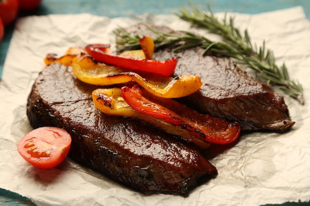 Composizione con gustosa carne arrosto su foglio di carta pomodori e rametti di rosmarino su fondo di legno