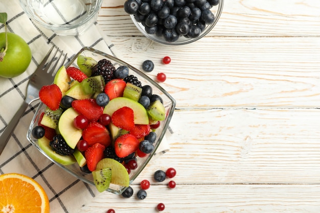 Composizione con la tazza di insalata di frutta fresca sulla tavola di legno bianca