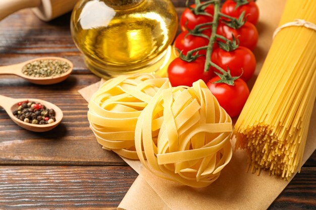 Composizione con pasta, pomodori, matterello, spezie e olio d'oliva su fondo di legno, spazio per testo e primo piano