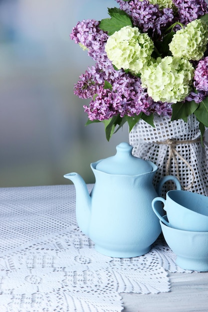 Composizione con set da tè e bellissimi fiori primaverili in vaso su tavola di legno su sfondo luminoso