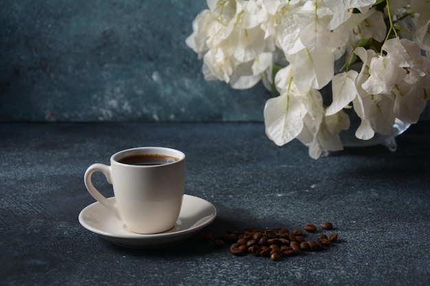 Composizione con tazza di caffè bianca, fagioli e fiori come sfondo