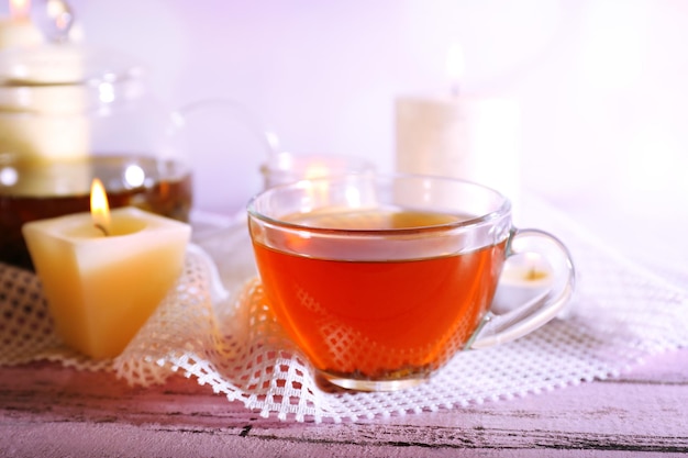 Composizione con tè in tazza e teiera e candele sul tavolo su sfondo chiaro