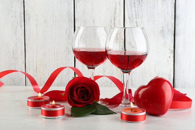 Composizione con vino rosso in vetro, rose rosse e cuore decorativo su fondo in legno colorato