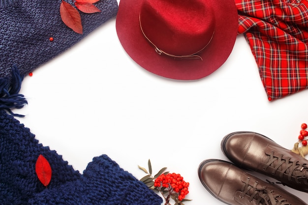 Composizione cornice moda autunno. Giaccone piatto con eleganti abiti e accessori femminili autunnali: stivali, cappello bordeaux, un'accogliente sciarpa a maglia, maglione caldo e gonna scozzese.