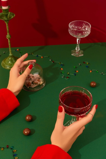 Composizione creativa del nuovo anno di Natale con le mani della donna e un bicchiere di champagne rosso sul tavolo verde