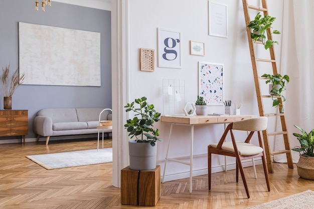 Composizione creativa dell'elegante design degli interni dell'home office scandi con cornici, scrivania in legno, sedia, piante e accessori. Pareti neutre, pavimento in parquet.