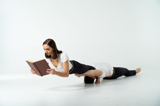 Composizione creativa della donna che mantiene l'equilibrio sulle mani dell'uomo e sul libro di lettura