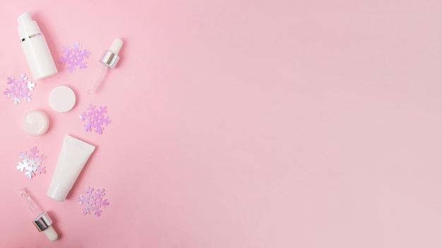 Composizione da contenitori di cosmetici vuoti e fiocchi di neve scintillanti sullo sfondo rosa con neve Banner grande con spazio per la copia