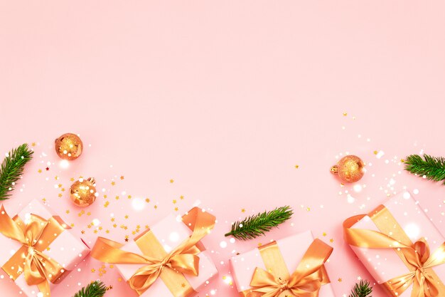 Composizione decorativa di Natale con confezione regalo di carta, palle di Natale in oro e fiocco in nastro d'oro su uno sfondo rosa.