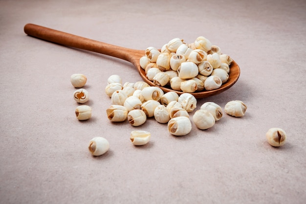 Composizione dei semi di loto crudi in cucchiaio di legno su fondo marrone.