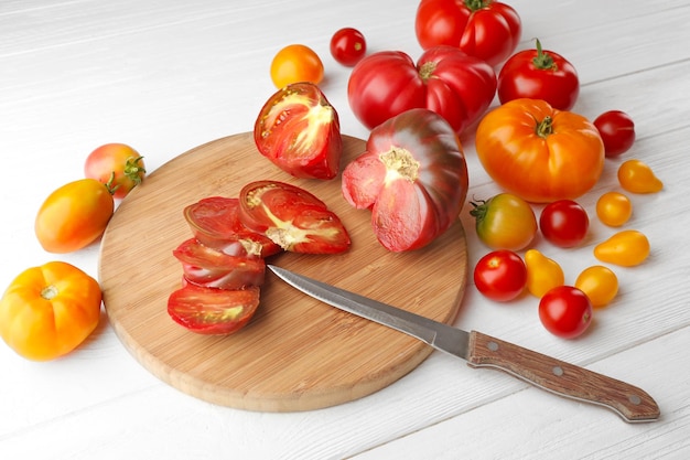 Composizione del coltello e del tagliere dei pomodori su fondo di legno bianco