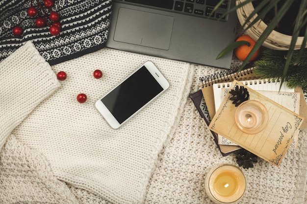 Composizione dell'area di lavoro invernale e autunnale, concetto di mockup piatto, smartphone, taccuino, sfondo di maglione lavorato a maglia con candela, foto di design di blogger