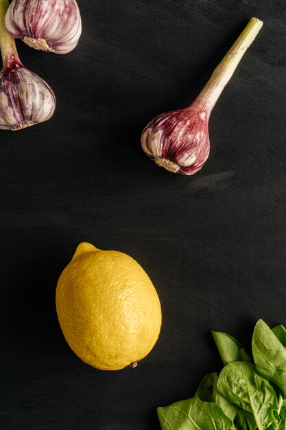 Composizione di aglio e limone su uno sfondo nero con erbe fresche