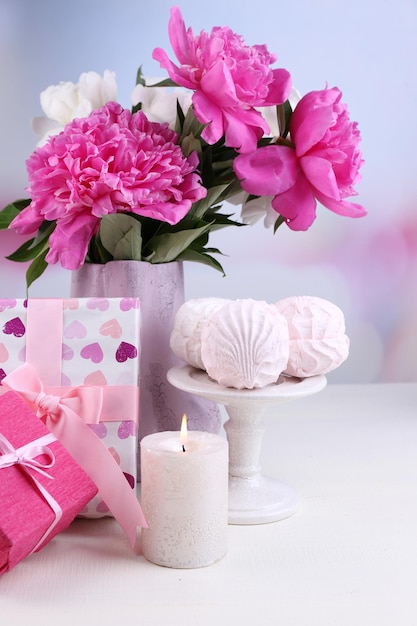 Composizione di bellissime peonie in vaso, tè in tazza e marshmallow, su tavola, su sfondo chiaro
