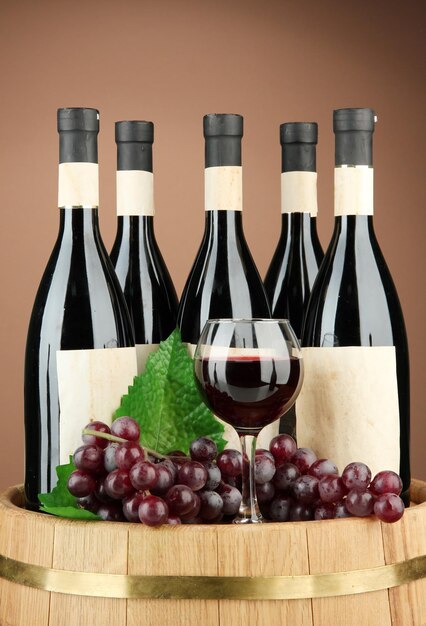 Composizione di bicchieri di bottiglie di vino e botte di legno di uva su sfondo marrone