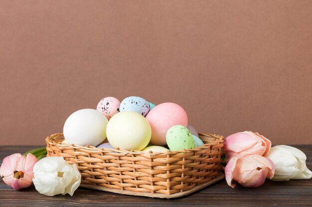 Composizione di Buona Pasqua Uova di Pasqua in cesto su tavolo colorato con tulipani gialli Uova colorate naturali sullo sfondo con spazio di copia