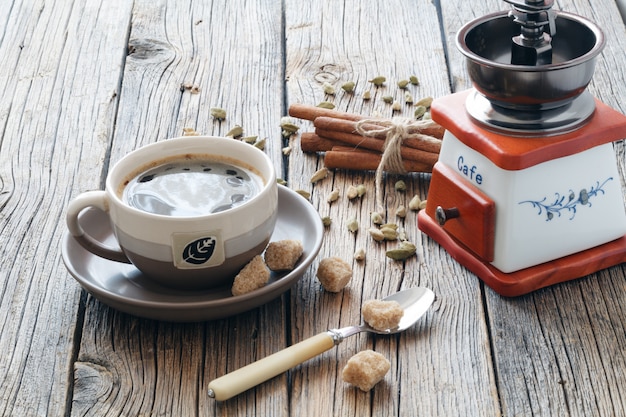 Composizione di caffè nero caldo in una tazza, zucchero di canna, chicchi di caffè e semi di cardamomo su un tavolo di legno. Luce speciale.