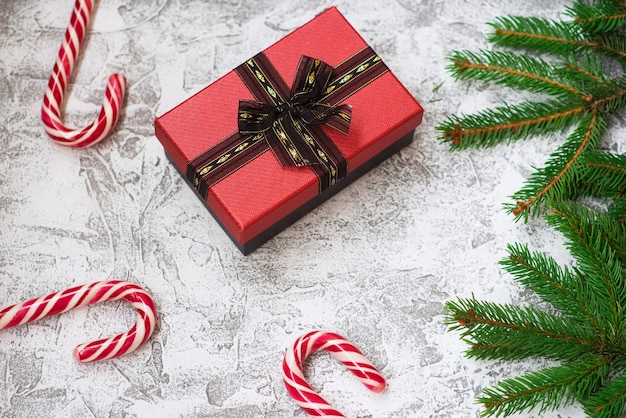 Composizione di Capodanno o Natale di rami verdi di abete rosso, regalo e lecca-lecca di Natale su uno sfondo materico luminoso. Disposizione piatta, layout, cornice, spazio di copia