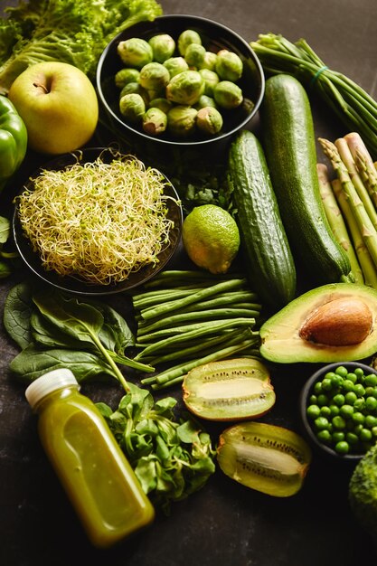 Composizione di cibo verde sano con avocado, broccoli, mela, frullato, cetriolo, asparagi, kiwi, posto su sfondo scuro, vista dall'alto