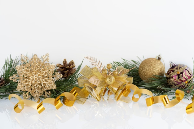 Composizione di decorazioni natalizie palline d'oro, fiocco di neve, campane e coni con rami di pino su bianco