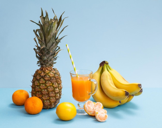 Composizione di frutti tropicali Ananas, banane, mandarini e limone con bicchiere di succo di frutta